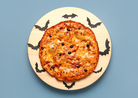 Wooden board of tasty pizza with olives and paper bats for Halloween party on blue backgroundの写真素材