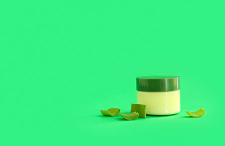 Jar of cosmetic cream with aloe vera leaves on green backgroundの写真素材