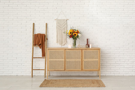 Wooden cabinet with bouquet of autumn flowers and burning candles near white brick wallの写真素材