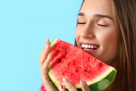 Young woman eating fresh watermelon on blue background, closeupの写真素材