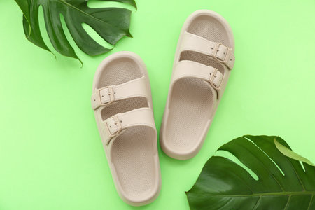 Pair of beige flip flops and tropical leaves on green background