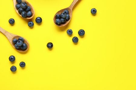 Wooden spoons with fresh blueberries on yellow backgroundの写真素材