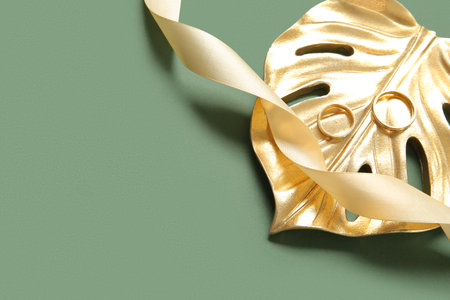 Golden monstera leaf with rings and ribbon on green backgroundの写真素材