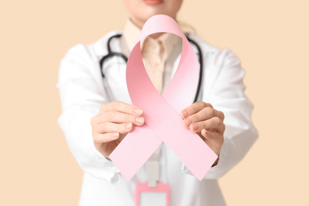 Female doctor with pink ribbon on beige background, closeup. Breast cancer awareness conceptの写真素材