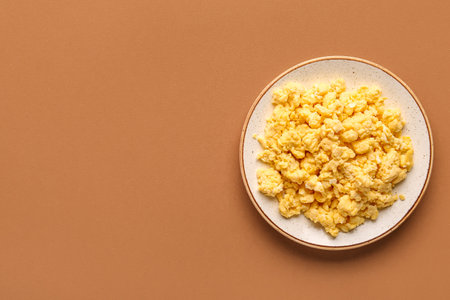 Plate of tasty scrambled eggs on brown backgroundの写真素材
