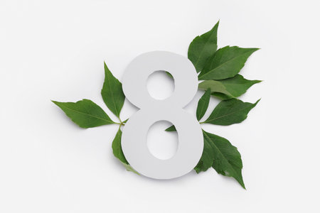 Green leaves with paper number eight on white background
