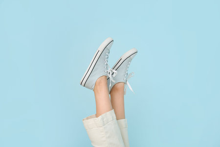 Female legs in stylish gumshoes on color background