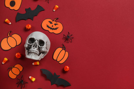 Composition with tasty candy corns, skull and Halloween decor on red backgroundの写真素材