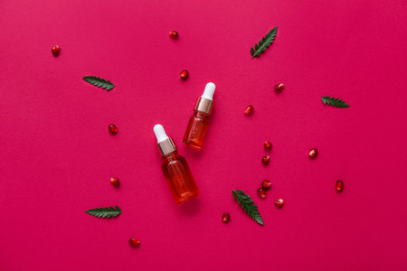 Composition with bottles of essential oil, pomegranate seeds and plant leaves on color backgroundの写真素材