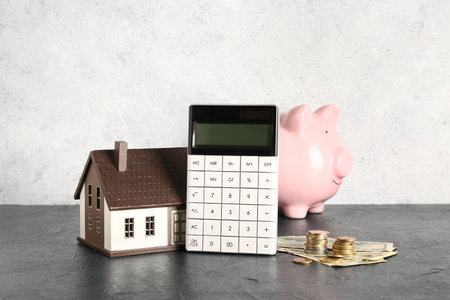 Calculator with piggy bank, house model and money on black tableの写真素材