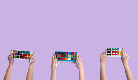 Female hands with watercolor paints on lilac backgroundの写真素材