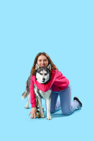 Happy young woman with husky dog on light blue backgroundの写真素材