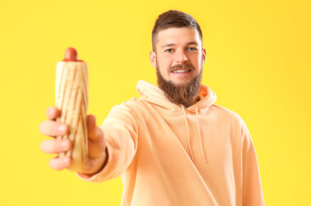 Portrait of happy young man with tasty hot dog on yellow backgroundの写真素材