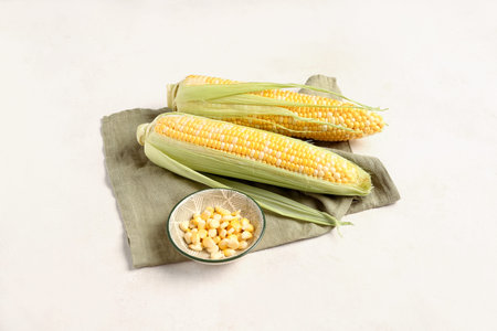 Fresh corn cobs and bowl with seeds on white background