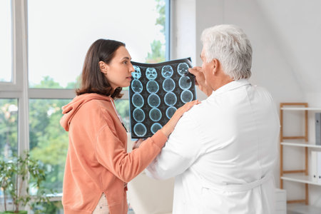 Senior doctor showing x-ray scan to young female patient in rehabilitation center