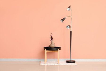 Standard lamp and vase with eucalyptus branches on small table near pink wall