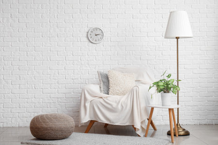 Armchair with blanket, standard lamp and houseplant near white brick wallの写真素材