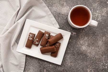 Plate with tasty chocolate covered coconut candies and cup of tea on gray backgroundの写真素材