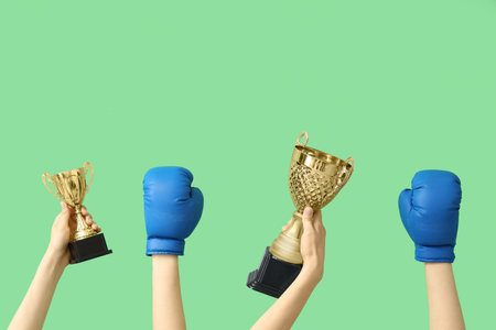Female hands with gold cups and boxing gloves on green backgroundの写真素材