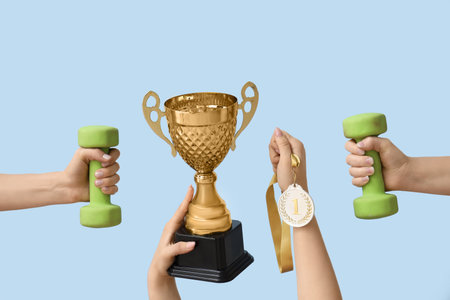 Female hands with gold cup, medal and dumbbells on blue backgroundの写真素材