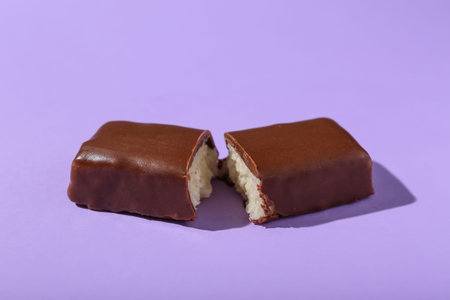 Halves of tasty chocolate covered coconut candy on lilac backgroundの写真素材