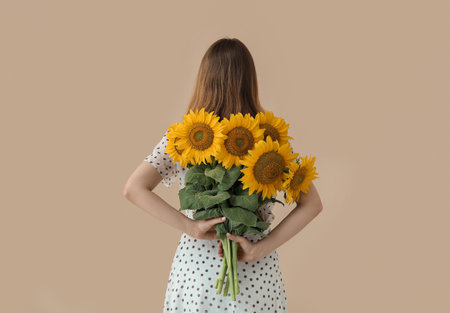 Young woman with beautiful sunflowers on beige background, back viewの写真素材