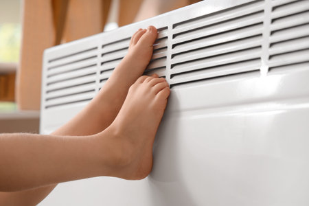 Barefoot little girl warming legs near radiator at home, closeup