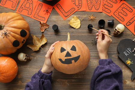 Woman painting Halloween pumpkin at wooden tableの写真素材