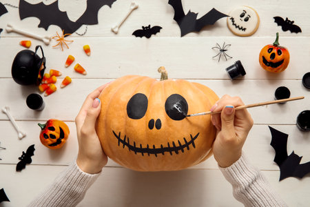 Woman painting Halloween pumpkin at white wooden tableの写真素材