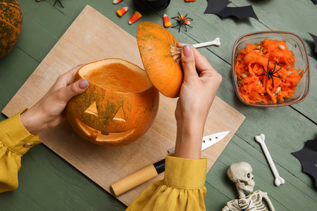 Woman with carved Halloween pumpkin at green wooden tableの写真素材