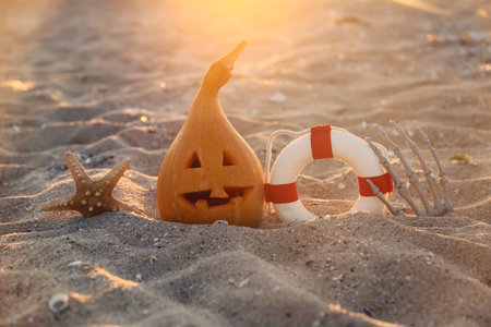 Carved pumpkin for Halloween with lifebuoy, starfish and skeleton hand on beachの写真素材