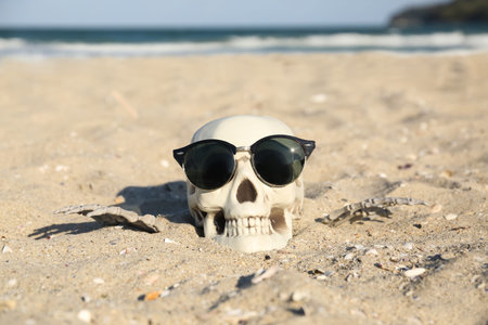 Skull for Halloween with stylish sunglasses and skeleton hands on beach