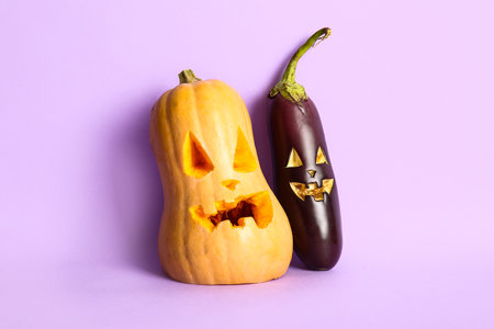Carved pumpkin and eggplant for Halloween on lilac backgroundの写真素材