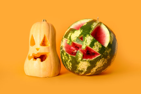 Carved pumpkin and watermelon for Halloween on orange backgroundの写真素材