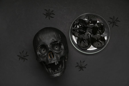 Halloween composition with skull, spiders and licorice candies on black background