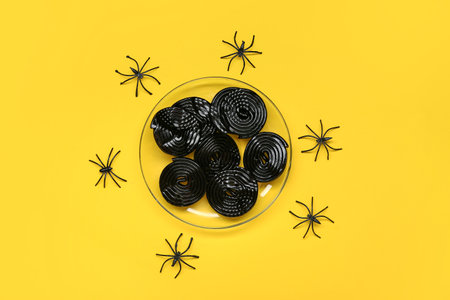 Halloween composition with sweet licorice candies and spiders on yellow backgroundの写真素材
