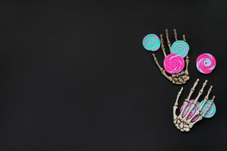 Halloween composition with skeleton hands and sweet candies on black background