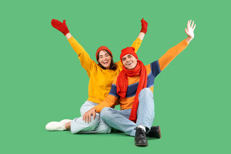Happy young couple in warm clothes sitting on green backgroundの写真素材