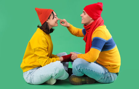 Happy young couple in warm clothes sitting on green backgroundの写真素材