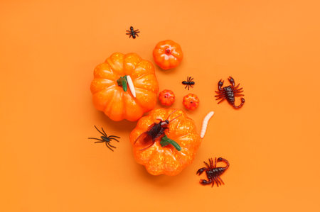 Halloween composition with pumpkins and candy bugs on orange backgroundの写真素材