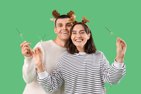 Happy young couple in Christmas reindeer horns with sparklers on green backgroundの写真素材