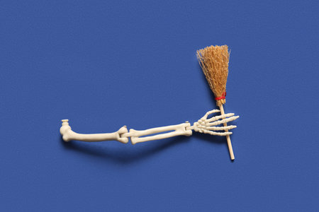 Halloween skeleton hand with broom on blue background