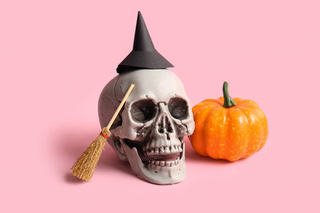 Halloween composition with skull, witch hat, pumpkin and broom on pink backgroundの写真素材