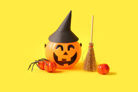 Halloween composition with pumpkins, witch hat and broom on yellow backgroundの写真素材