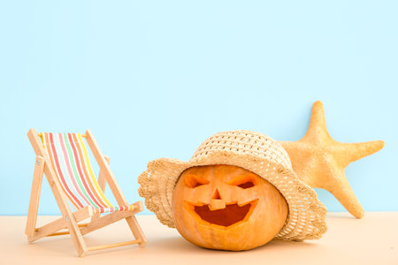 Carved pumpkin for Halloween with stylish hat and deck chair on blue backgroundの写真素材