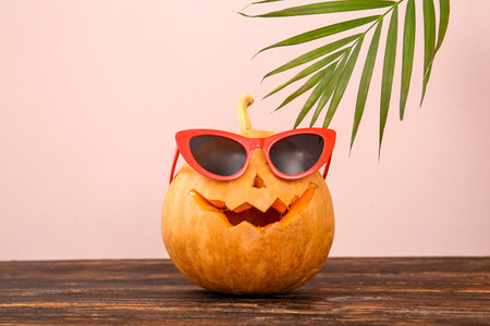 Carved pumpkins for Halloween with stylish sunglasses on table near beige wallの写真素材