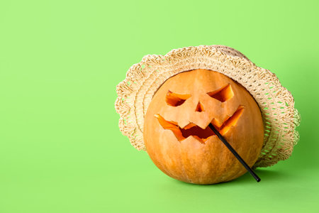 Carved pumpkin for Halloween with stylish hat and straw on green backgroundの写真素材