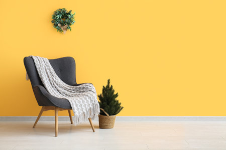 Gray armchair with blanket and small Christmas tree near orange wallの写真素材