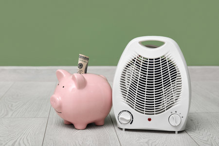 Electric fan heater and piggy bank on floor. Heating seasonの写真素材