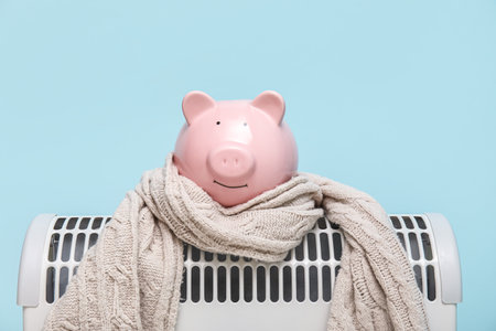 Electric convector heater, piggy bank and scarf on blue background. Heating seasonの写真素材